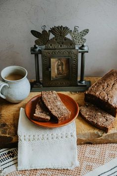 two slices of banana bread on a plate next to a cup of coffee and an antique clock