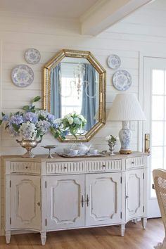 a white dresser with blue and white plates on it, next to a large mirror