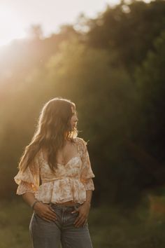 a woman standing in the grass with her hands on her hips and looking off into the distance