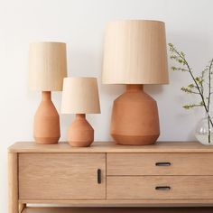 three vases and two lamps sitting on a dresser