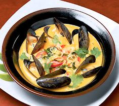 a bowl of soup with mussels and garnishes on the side