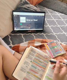 a person sitting on a bed with an open book and a laptop in front of them