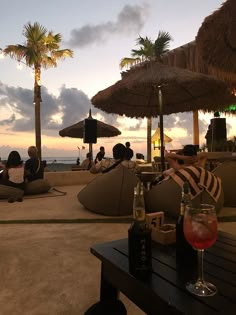 people are sitting on the beach with umbrellas and drinks in front of them as the sun sets