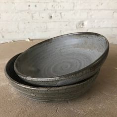 two gray bowls sitting on top of a table next to each other, one is empty and the other has a white brick wall behind it