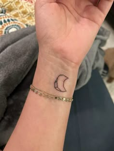 a woman's wrist with a small crescent tattoo on the left side of her arm