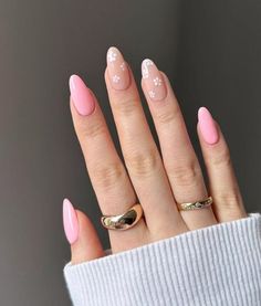 a woman's hand with pink and white nail polish on her nails, wearing a gold ring