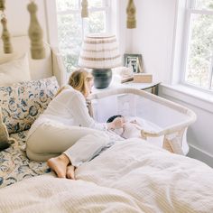 a woman sitting on top of a bed next to a baby in a crib