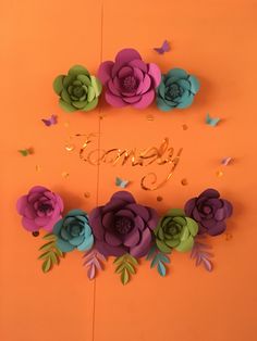 an orange background with purple and green paper flowers on the bottom, gold lettering that says happy