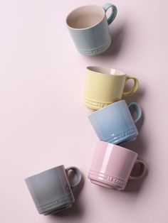 four coffee mugs sitting next to each other on a pink surface