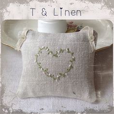 a heart - shaped embroidered pillow sitting on top of a table next to a cup and saucer