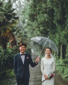 a bride and groom holding an umbrella on a path in the woods with greenery behind them