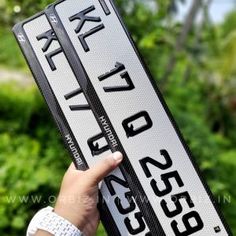 a person holding up a white and black street sign in front of some trees,