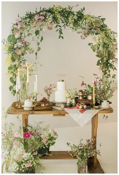 a table topped with lots of flowers and candles next to a wall covered in greenery