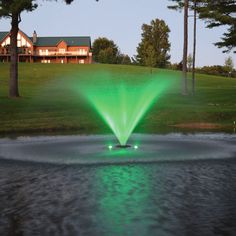 a green fountain spewing water into a pond in front of a large house