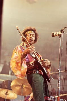 a man playing the guitar on stage with other instruments in front of him and an audience behind him