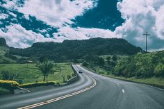 a car driving down an empty road with mountains in the background on a cloudy day