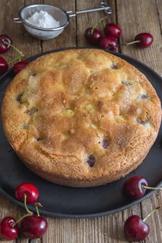 a cake sitting on top of a black plate next to cherries