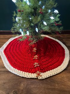 a crocheted christmas tree skirt on top of a wooden table next to a small pine tree