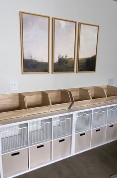 three pictures hang on the wall above white storage bins with drawers and dividers