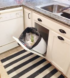 a trash can in the corner of a kitchen with a sink and dishwasher