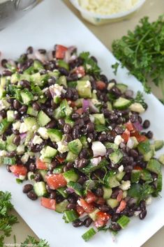 a salad with black beans, cucumber and tomatoes on a white cutting board