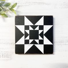 a black and white tile with an abstract design on the side next to a potted plant