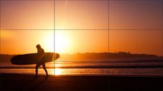 a person holding a surfboard walking on the beach at sunset with the sun in the background