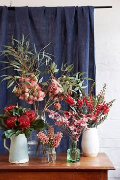 three vases filled with flowers sitting on top of a wooden table next to a blue curtain