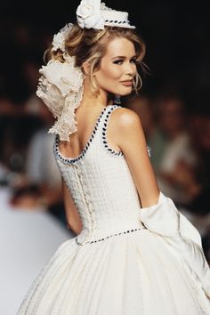 a woman is walking down the runway wearing a white dress and flower in her hair