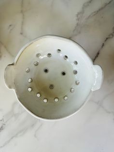 a white colander sitting on top of a marble counter next to a cup with holes in it