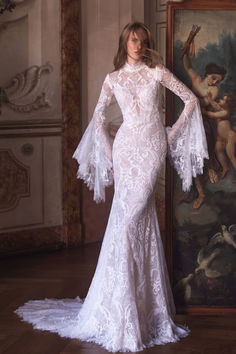 a woman in a white wedding dress standing next to a wall with paintings on it