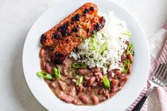 a white plate topped with meat, beans and rice