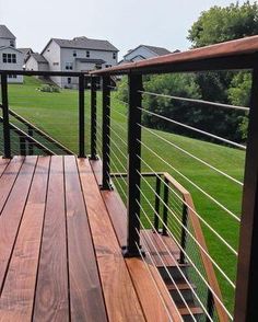 a wooden deck with metal railings in the middle of a grassy area next to houses