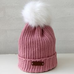 a pink beanie with a white pom - pom on the top, sitting on a table