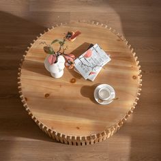 a wooden table topped with two white vases filled with flowers next to a book