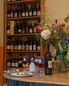 there are many bottles and glasses on the bar with flowers in vases next to it