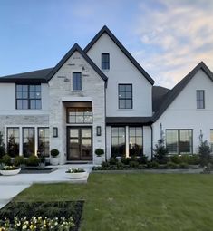 a large white house with lots of windows and plants in the front yard at dusk