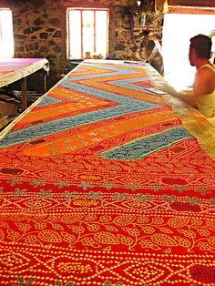 a woman sitting at a table working on an art project with red and orange colors