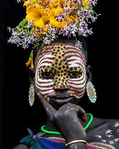 an african woman with painted face and flowers on her head, looking at the camera