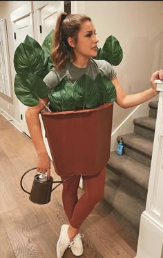 a woman in a potted plant costume is holding a watering can and looking at the stairs