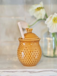 a honey jar with a straw in it next to some white flowers and vases