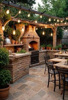 an outdoor dining area with patio furniture and lights strung over the fire place, surrounded by potted plants