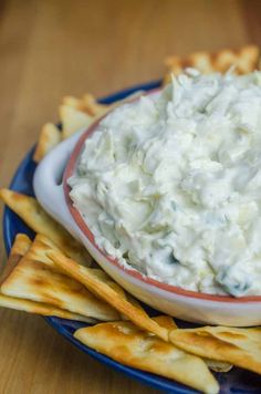 a blue plate topped with crackers and a bowl filled with white cream cheese dip