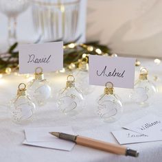 small glass ornaments with name tags on them sitting on a table next to a pen