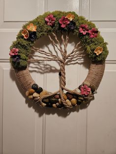 a wreath with flowers and rocks is hanging on a door frame in the shape of a tree