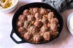 a skillet with meatballs and other food items on the table next to it