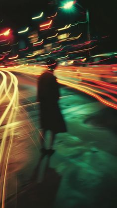 a blurry image of a person walking down the street at night with traffic lights in the background