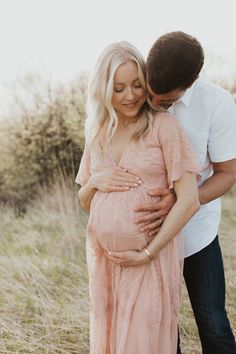 a pregnant woman hugging her husband's belly in the middle of an open field