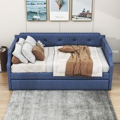 a blue couch sitting on top of a wooden floor next to two pictures above it