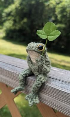 a small stuffed frog sitting on top of a wooden bench next to a green leaf